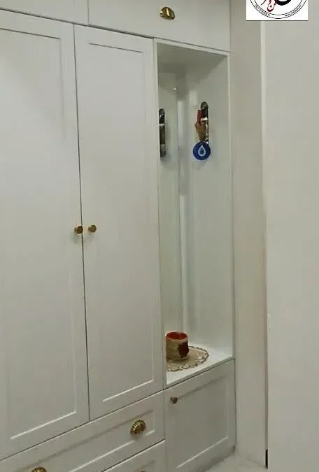 جالباسی نئوکلاسیک سفید با کلاف چوبی مشهود، شامل جا کفشی، آویز و نیمکت، در یک ورودی روشن و دکور شده.